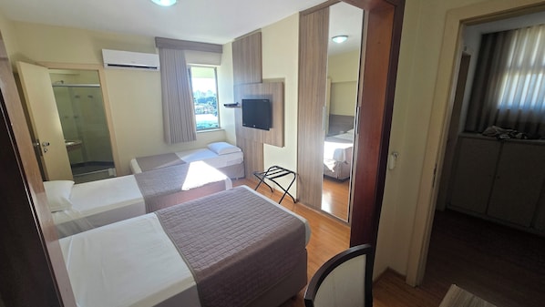 Habitación de hotel con dos camas, televisión, ventana con cortinas y vista a la ciudad.