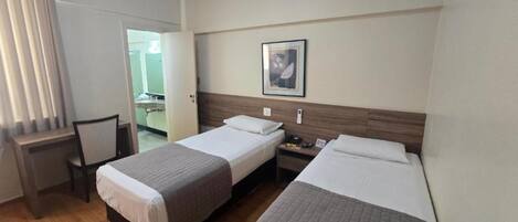 A hotel room with two beds, a desk, a chair, and a bathroom visible through an open door.