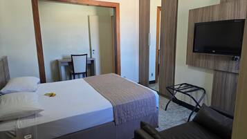 A hotel room with a bed, a desk, a chair, a TV, and a small table.