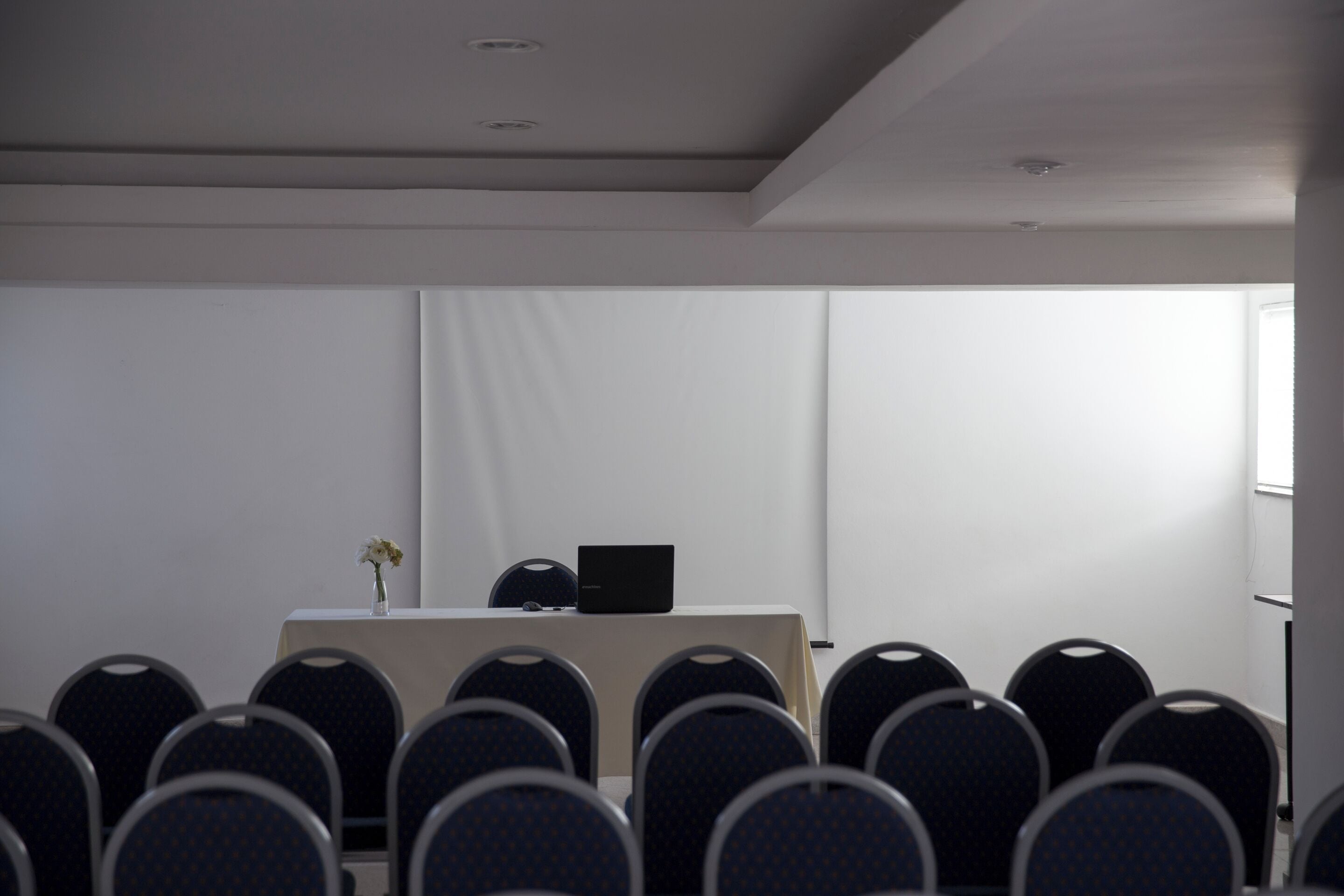 A conference room with rows of chairs, a table with a laptop, and a vase with flowers.