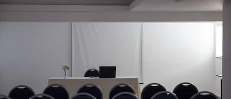 A conference room with rows of chairs, a table with a laptop, and a vase with flowers.