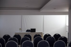 A conference room with rows of chairs, a table with a laptop, and a vase with flowers.