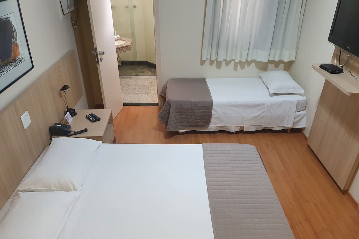 Hotelkamer met twee bedden, een bureau met telefoon, een televisie en een zichtbare badkamer door een open deur.