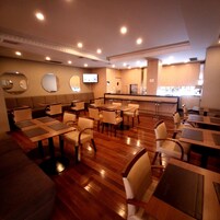 Un restaurante con mesas y sillas de madera, una zona de bar y un televisor montado en la pared.