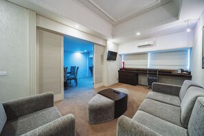 A modern living room with grey upholstered sofas, a dark coffee table, and a kitchen area with a TV and air conditioning unit. - Hotel Victoria Villa Curitiba By Nacional Inn (Curitiba)