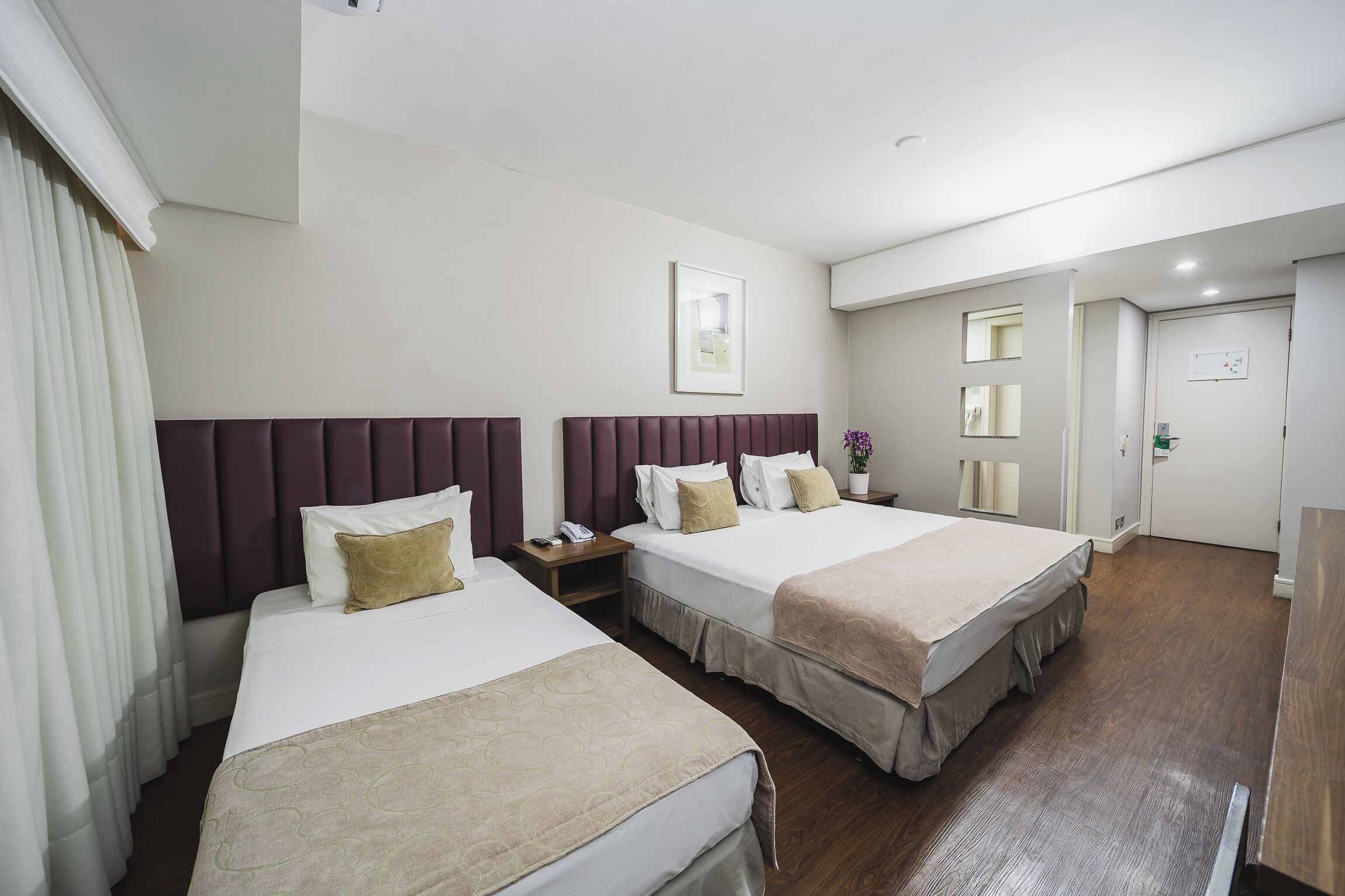 Una habitación de hotel con dos camas, una mesita de noche, un espejo y una puerta.
