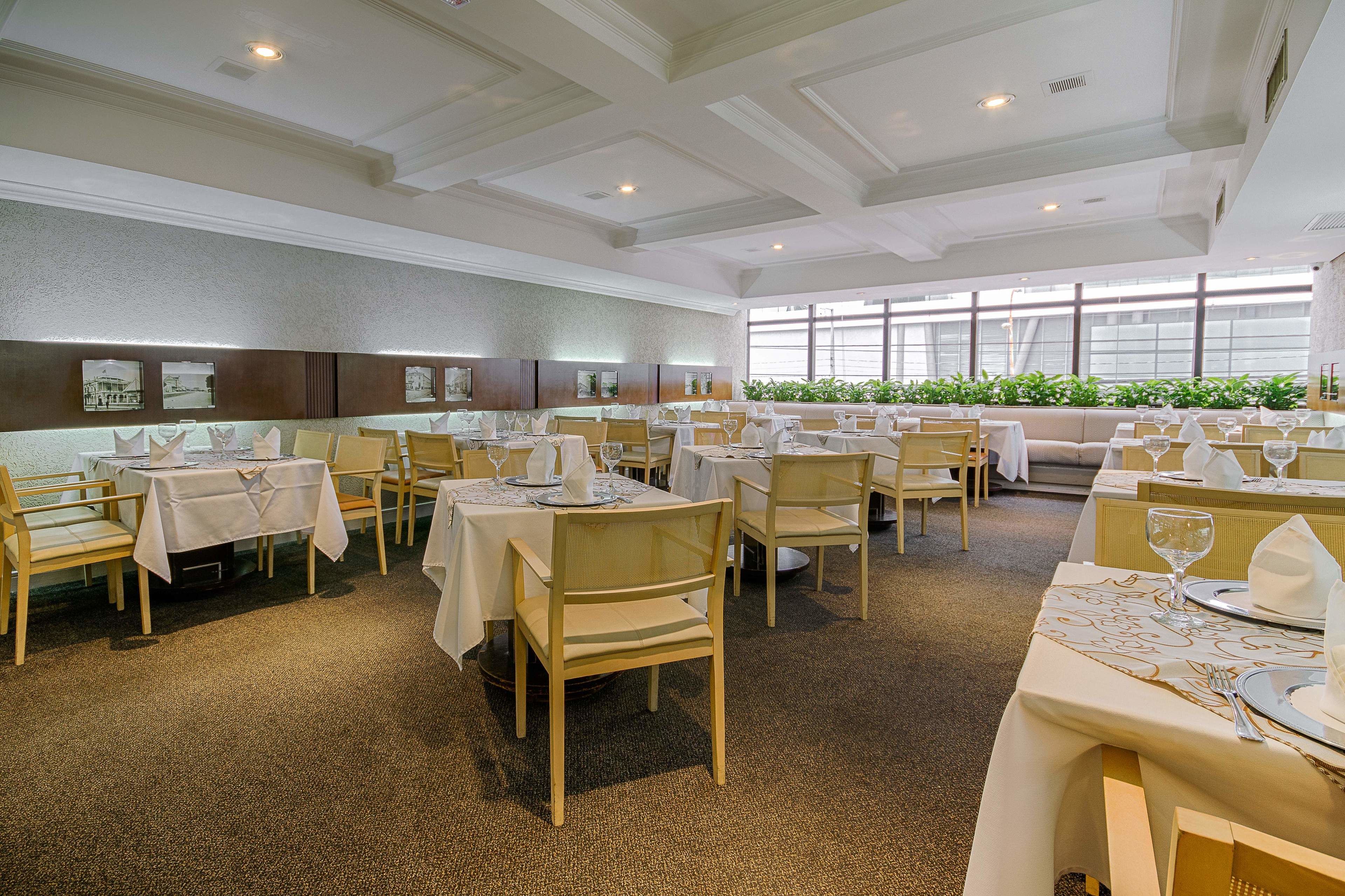 A spacious dining area with multiple tables and chairs, large windows, and a carpeted floor.