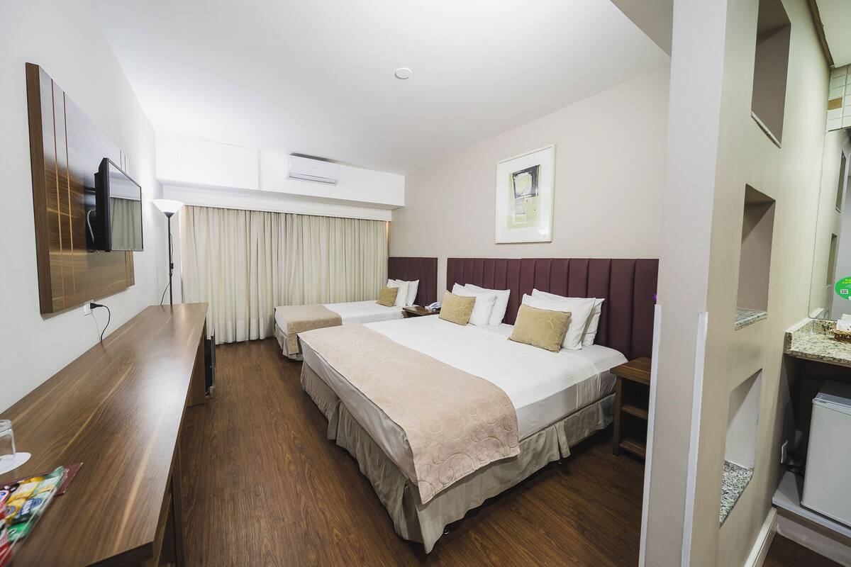 A hotel room with two beds, a desk, a flat-screen TV, an air conditioning unit, and a framed picture on the wall.