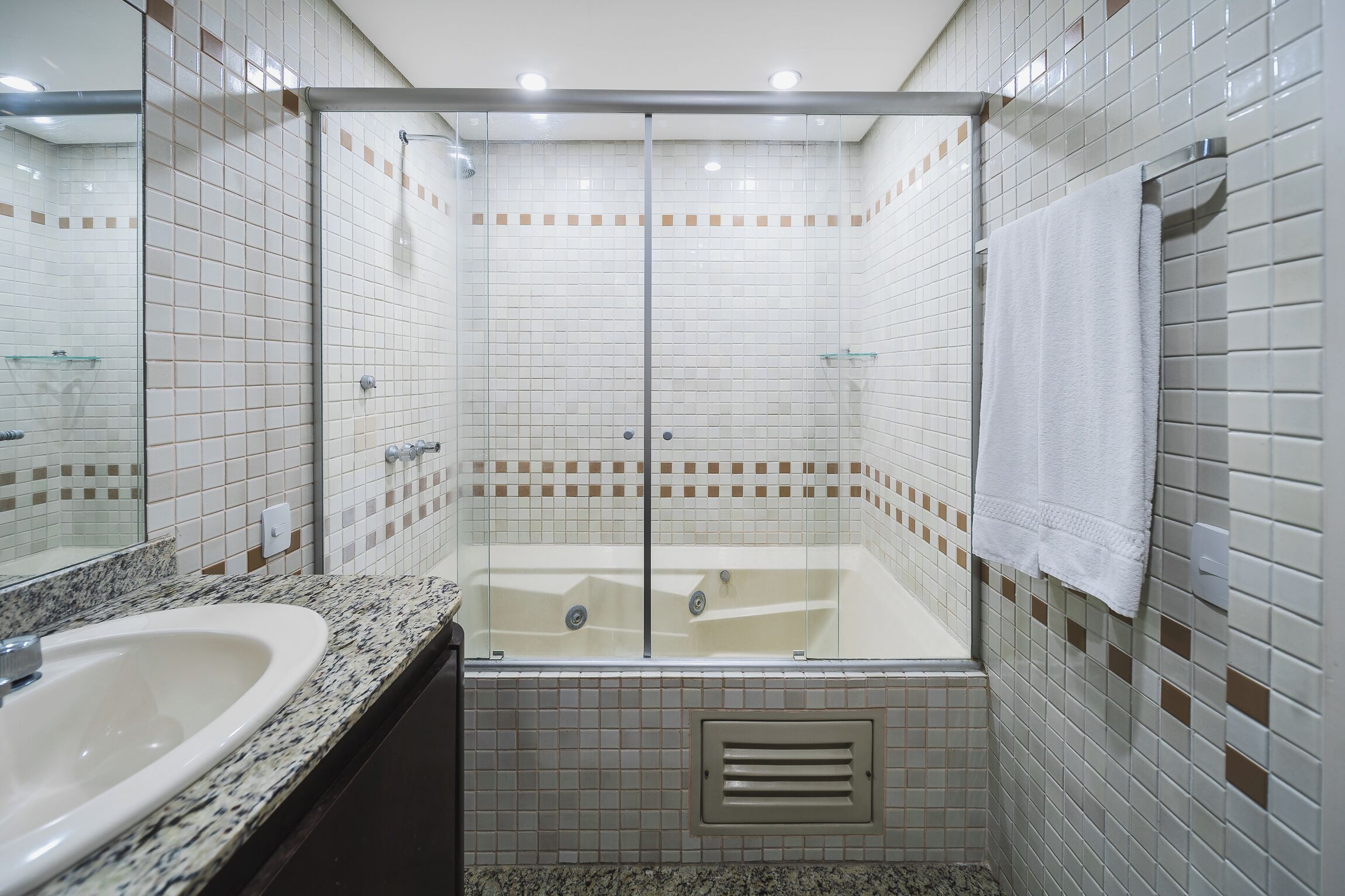 A bathroom with a glass-enclosed shower, a bathtub, and a granite countertop sink.
