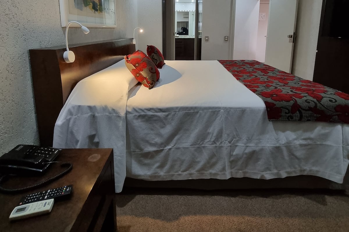 A hotel room with a bed, bedside table, and a painting on the wall.