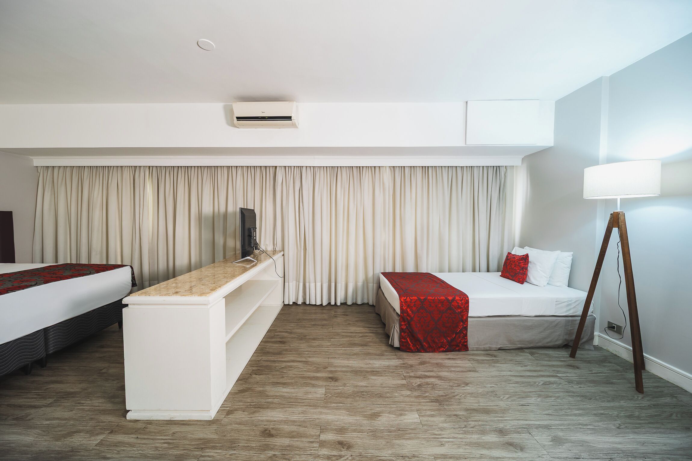 A hotel room with two beds, a TV, a desk, and a lamp.