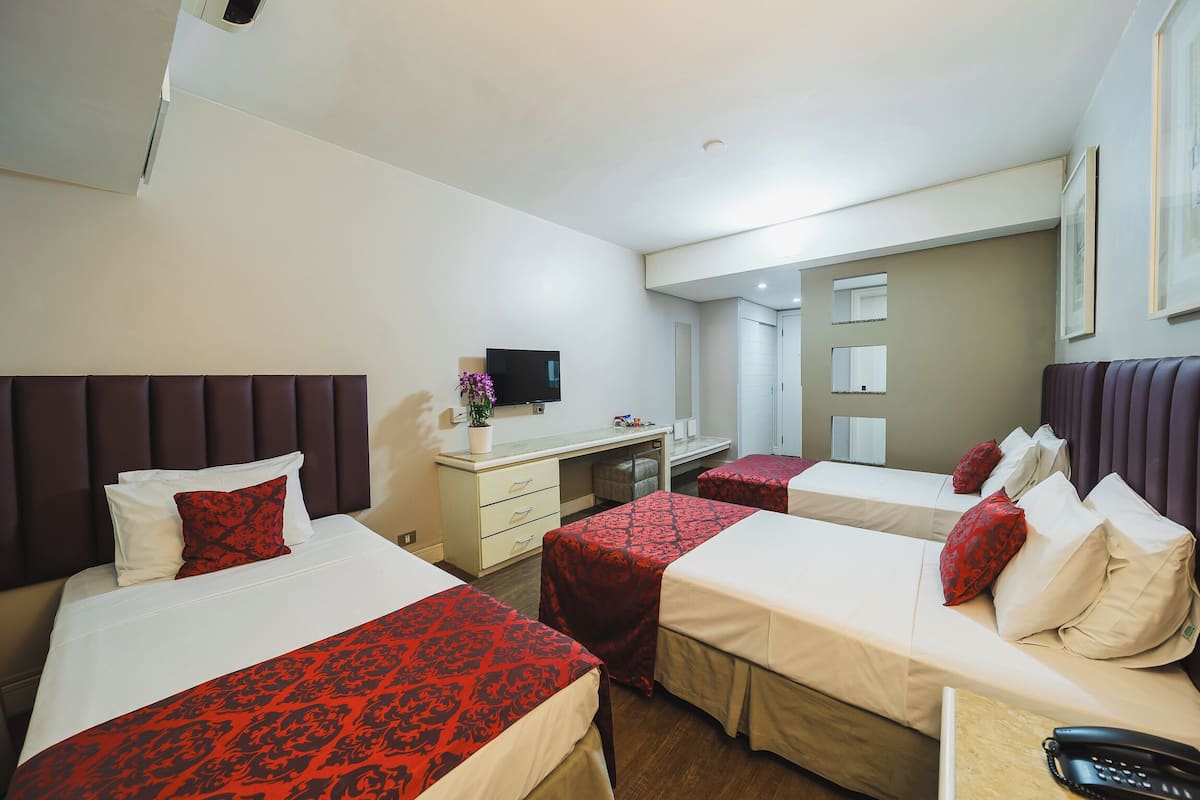 A hotel room with two beds, a desk, a chair, a TV, and a window.