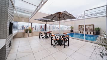 Terraço no telhado com piscina, área de estar ao ar livre e vista para a cidade.