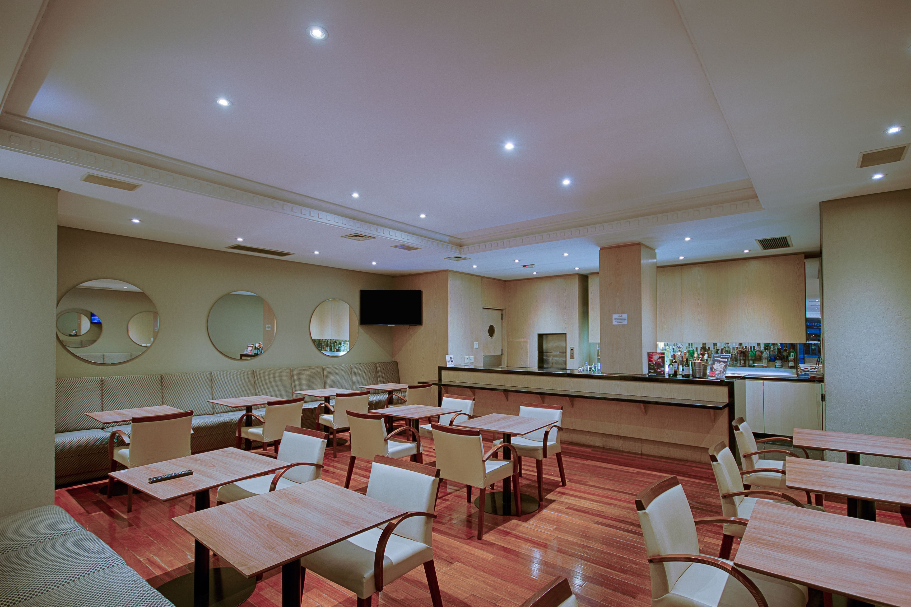 Um restaurante com várias mesas e cabines, área de bar e uma televisão na parede.