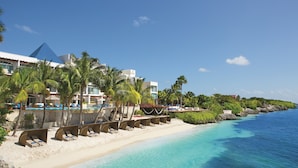 A beach resort with a clear blue ocean, palm trees, and a white building with a blue roof.