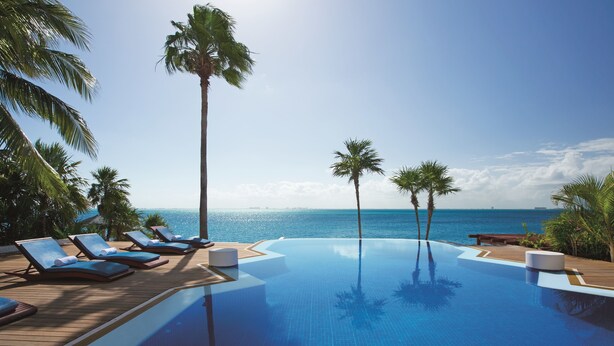 A infinity pool with lounge chairs and palm trees, overlooking the ocean.