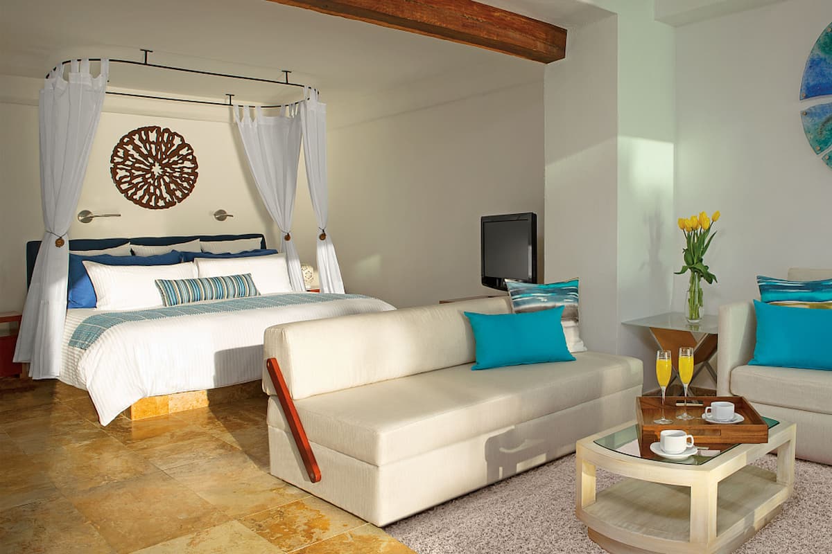 A hotel room with a bed, two sofas, a coffee table, a TV, and a decorative wall piece.