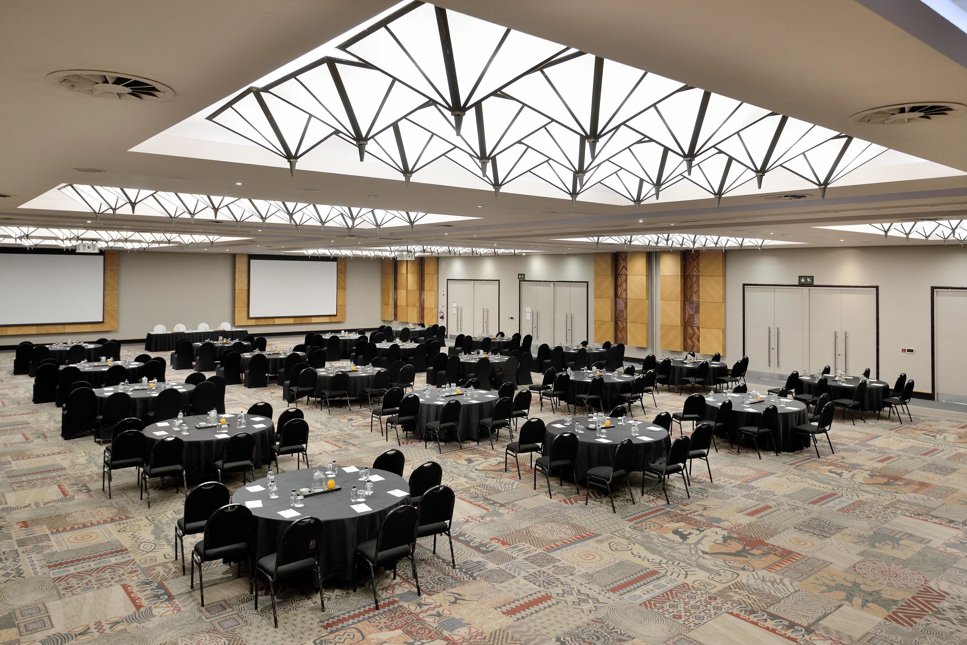 A conference room with multiple round tables, black chairs, and a patterned carpet.
