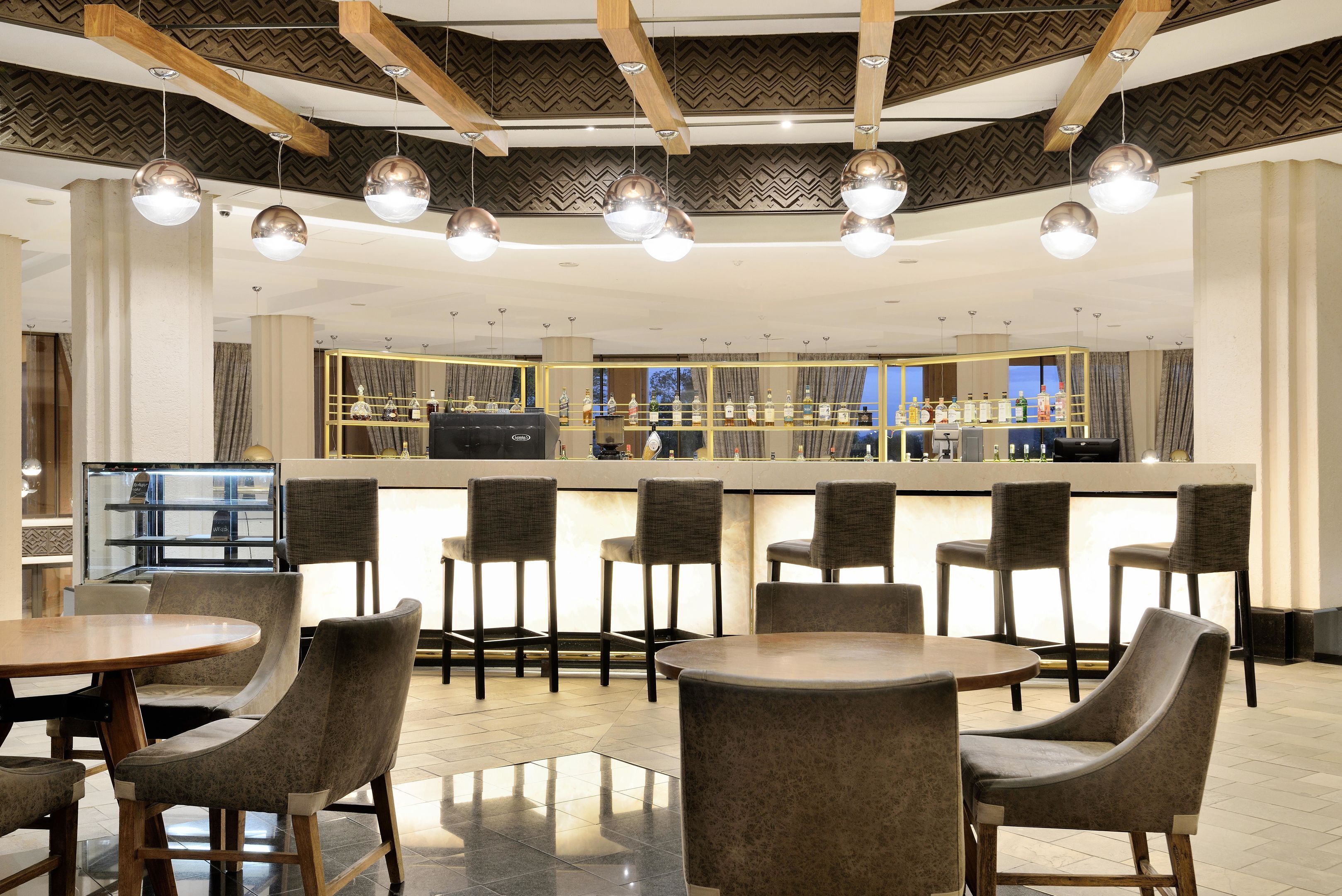 A modern bar area with round tables and chairs, a counter with a barista, and a patterned ceiling.