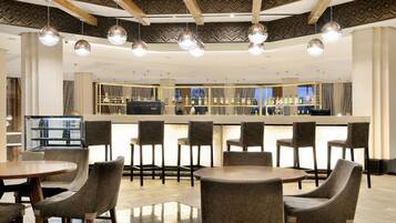 A modern bar area with round tables and chairs, a counter with a barista, and a patterned ceiling.