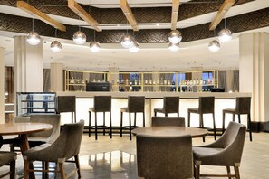 A modern bar area with round tables and chairs, a counter with a barista, and a patterned ceiling. - Windhoek Country Club (Windhoek)