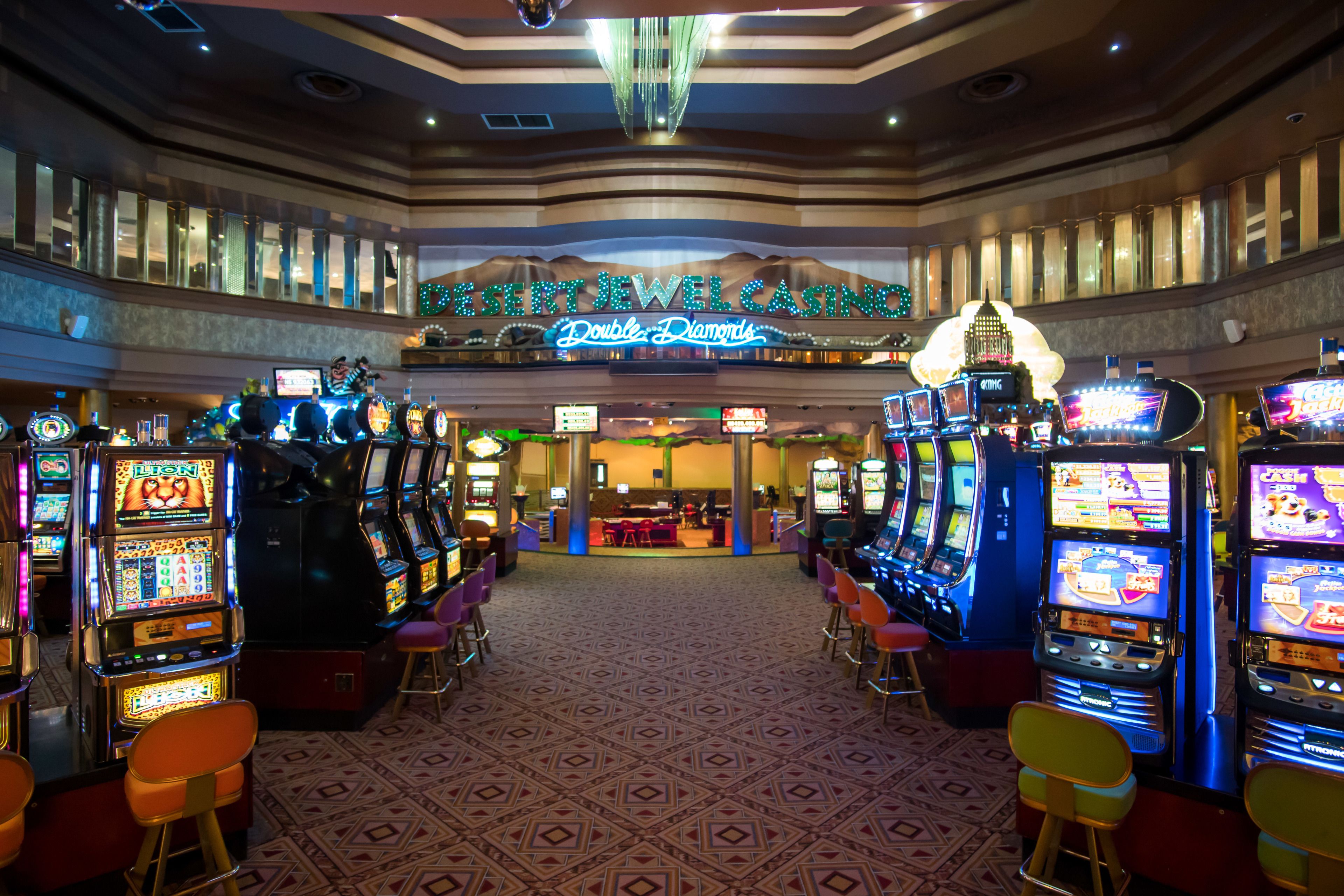 Un casino con múltiples máquinas tragamonedas y un letrero de neón que dice 'Desert Jewel Casino Double Diamonds'.