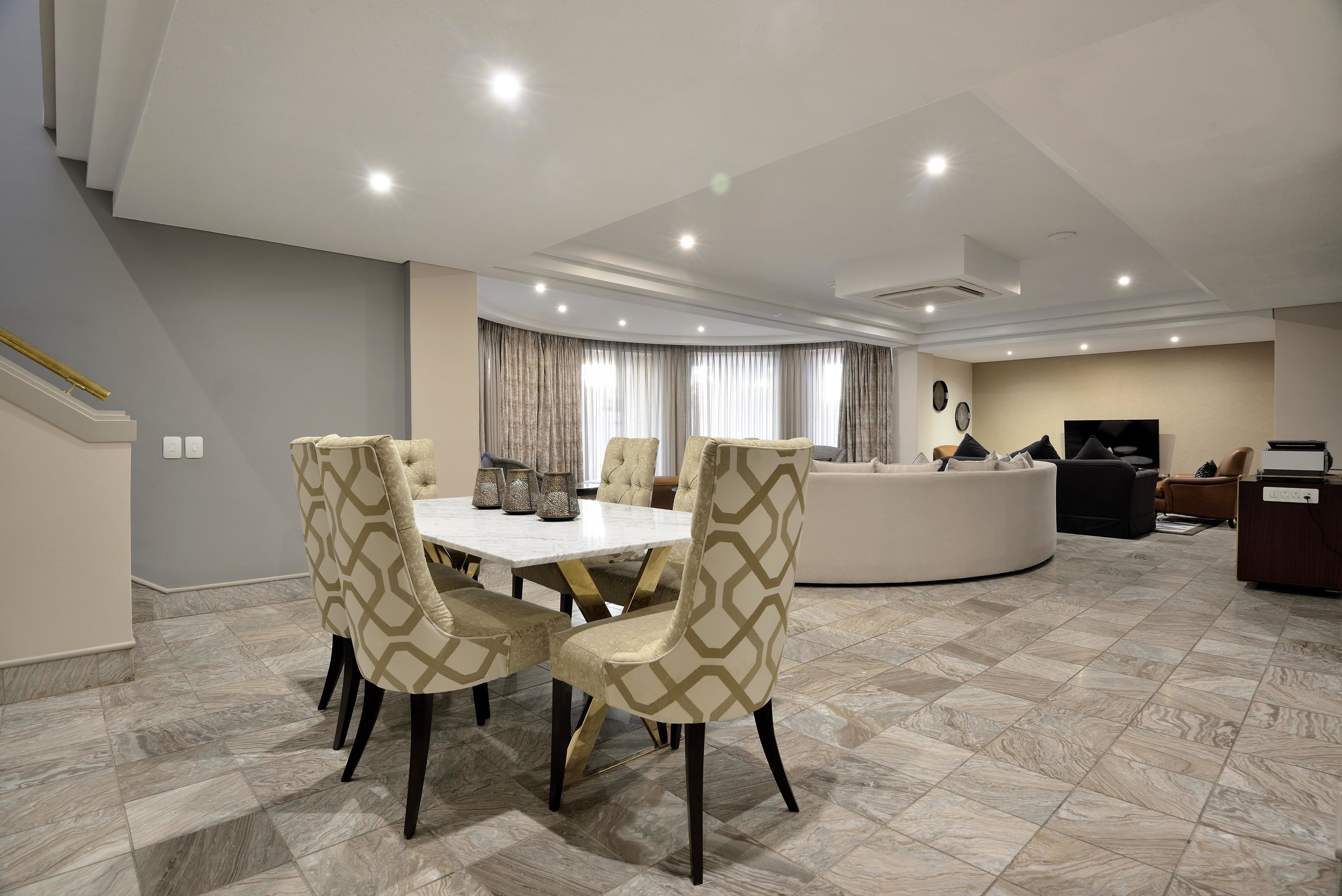A modern living room with a dining area, featuring a white table, patterned chairs, and a curved sofa.