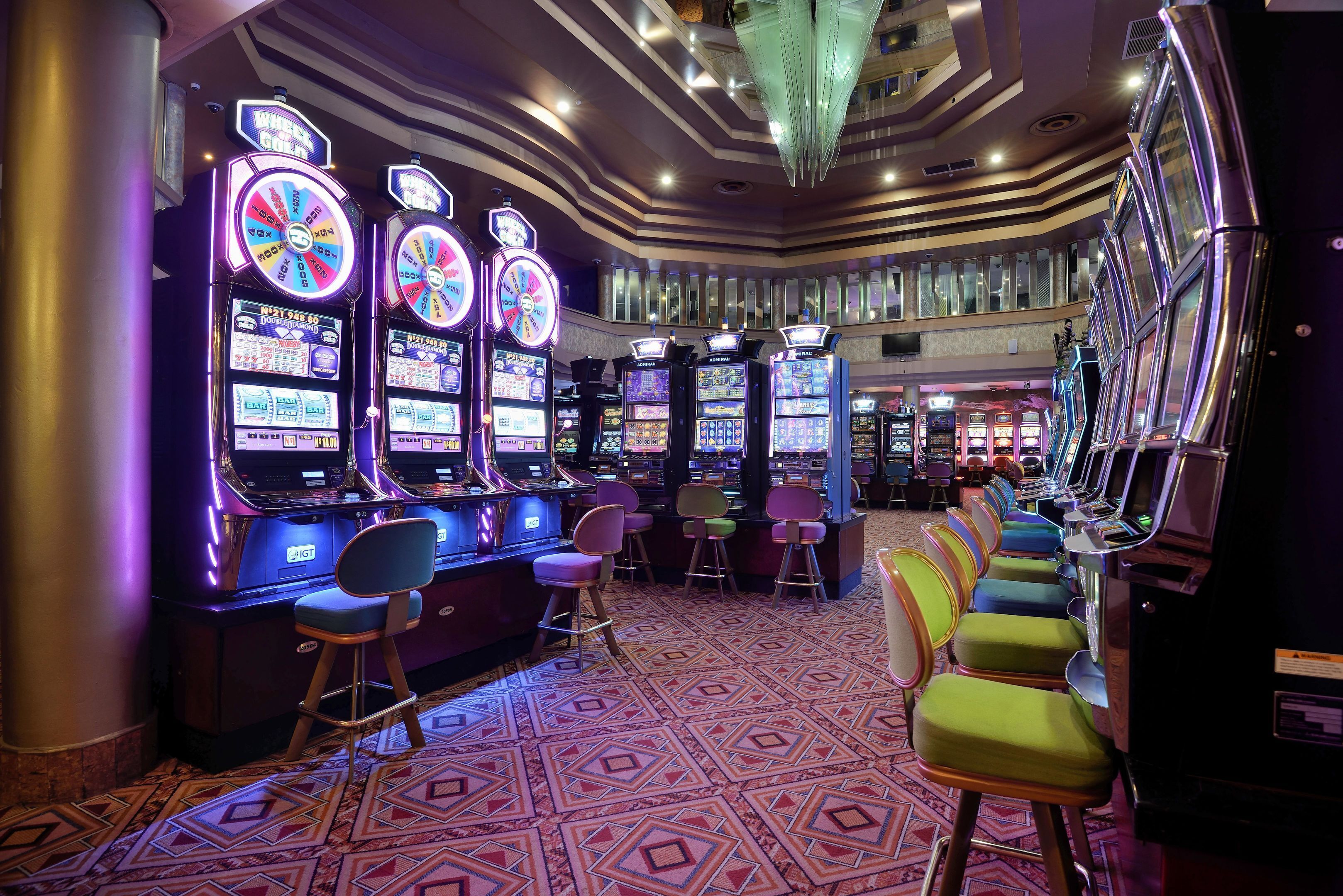 Un casino con numerosas máquinas tragamonedas, asientos de bar y una alfombra estampada.