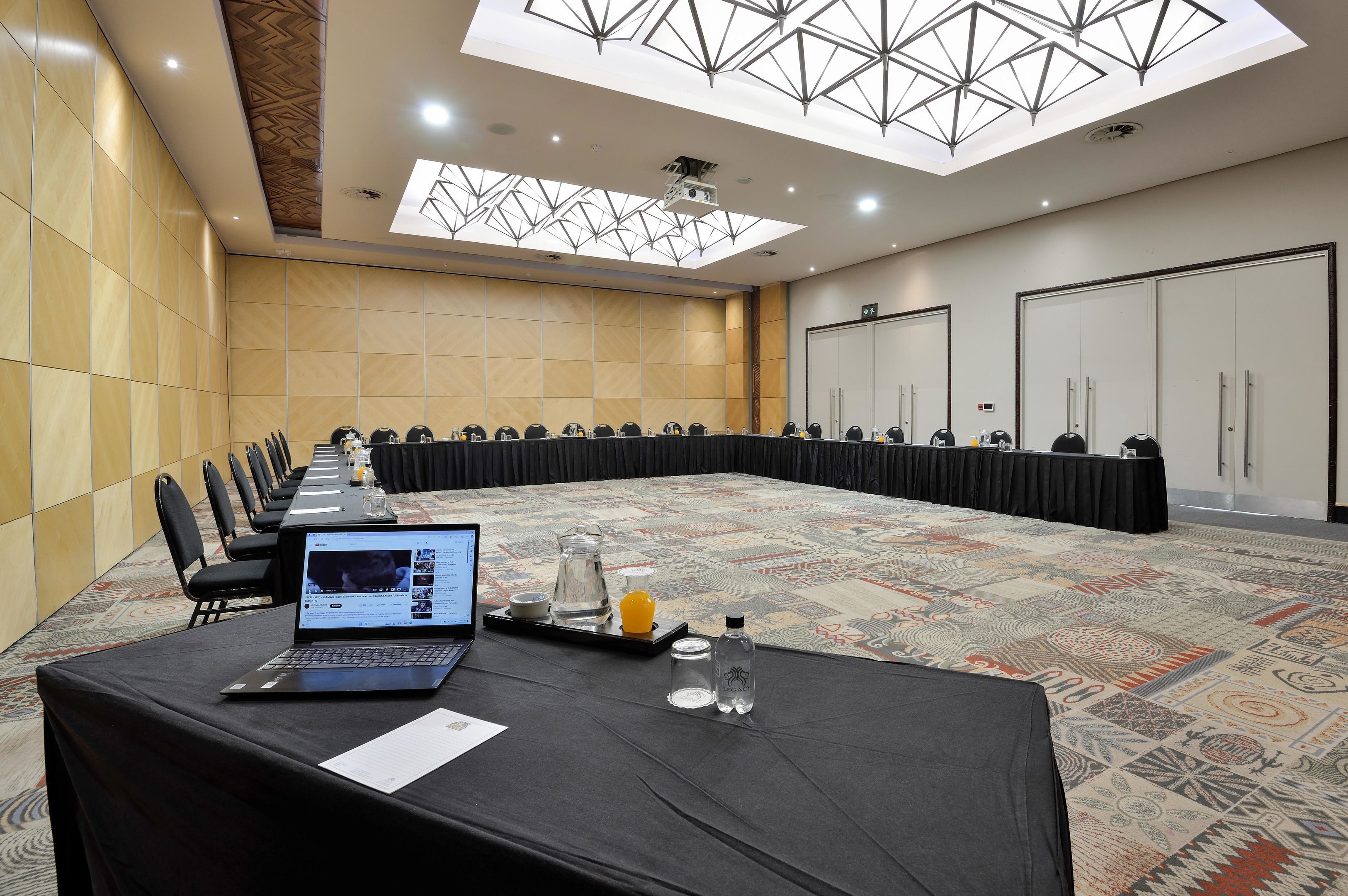 A conference room with a long table, chairs, a laptop, a projector, and a patterned carpet.