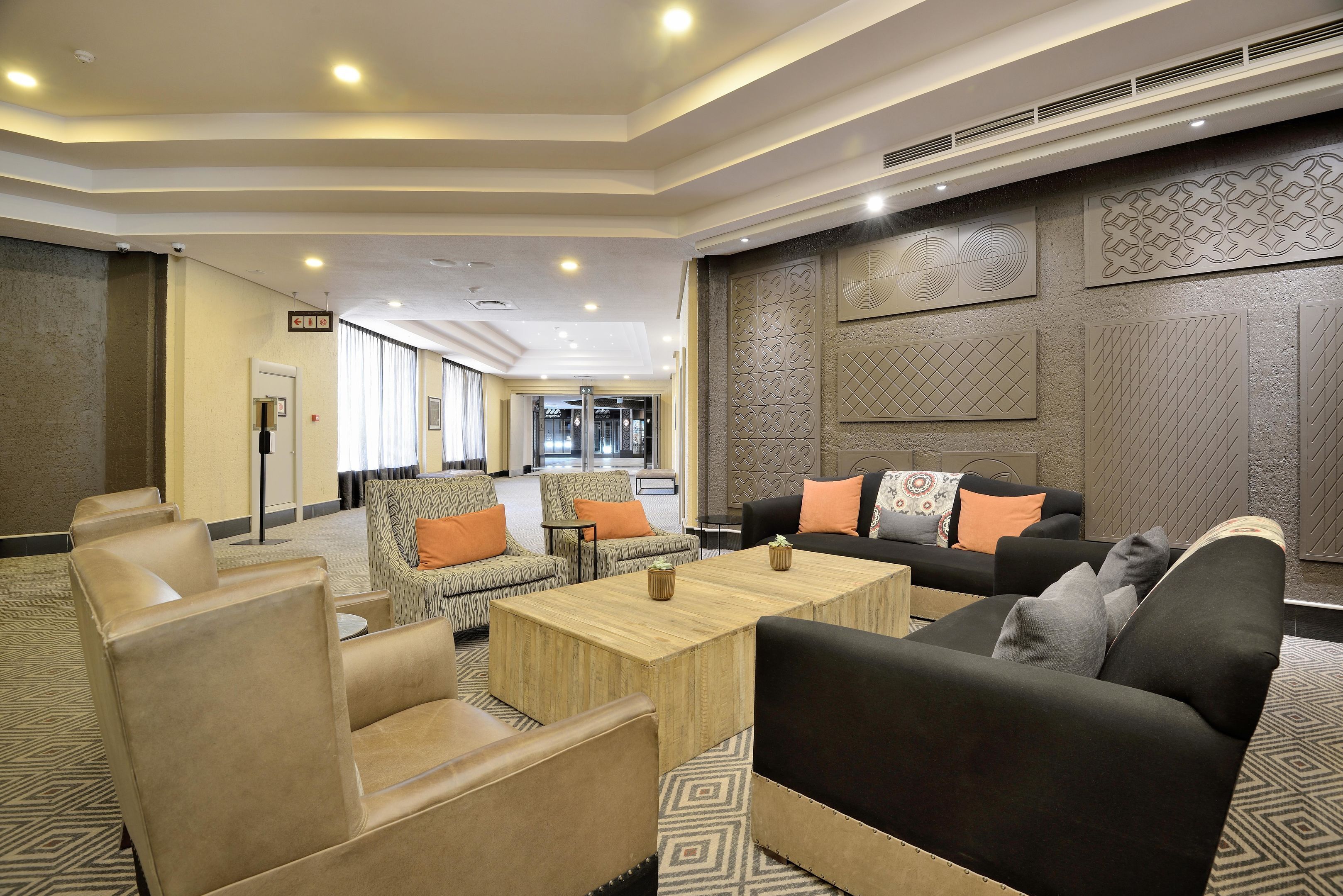 Un hall de hotel con sofás de cuero, una mesa de centro de madera, decoración mural estampada y una zona de recepción al fondo.