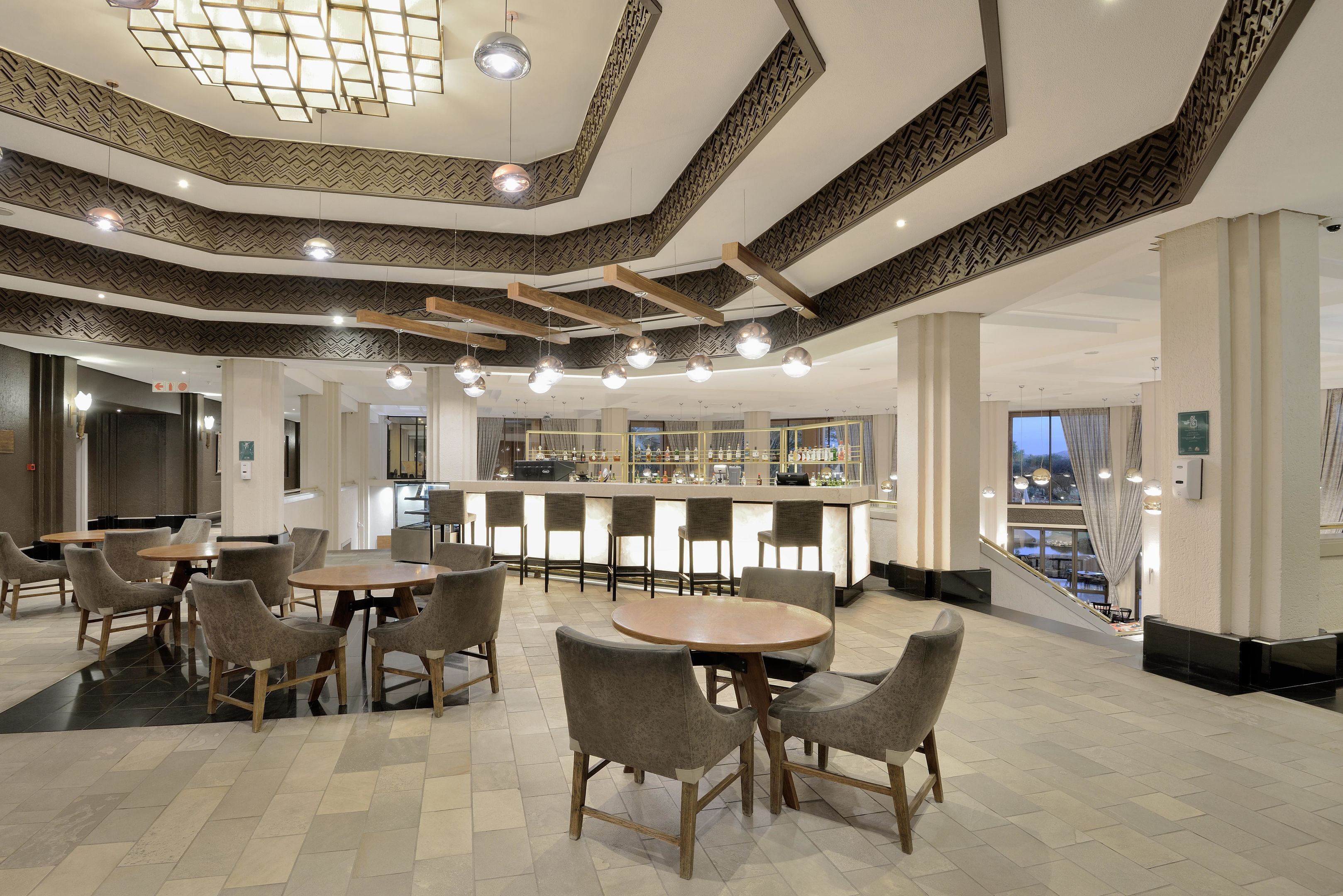A spacious lobby with a bar area, multiple seating arrangements, and a view of the outside.
