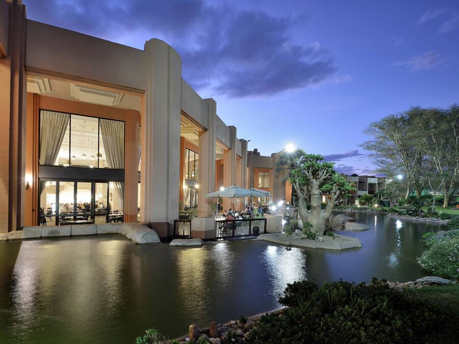 A hotel with a large outdoor pool, dining area, and well-lit entrance.