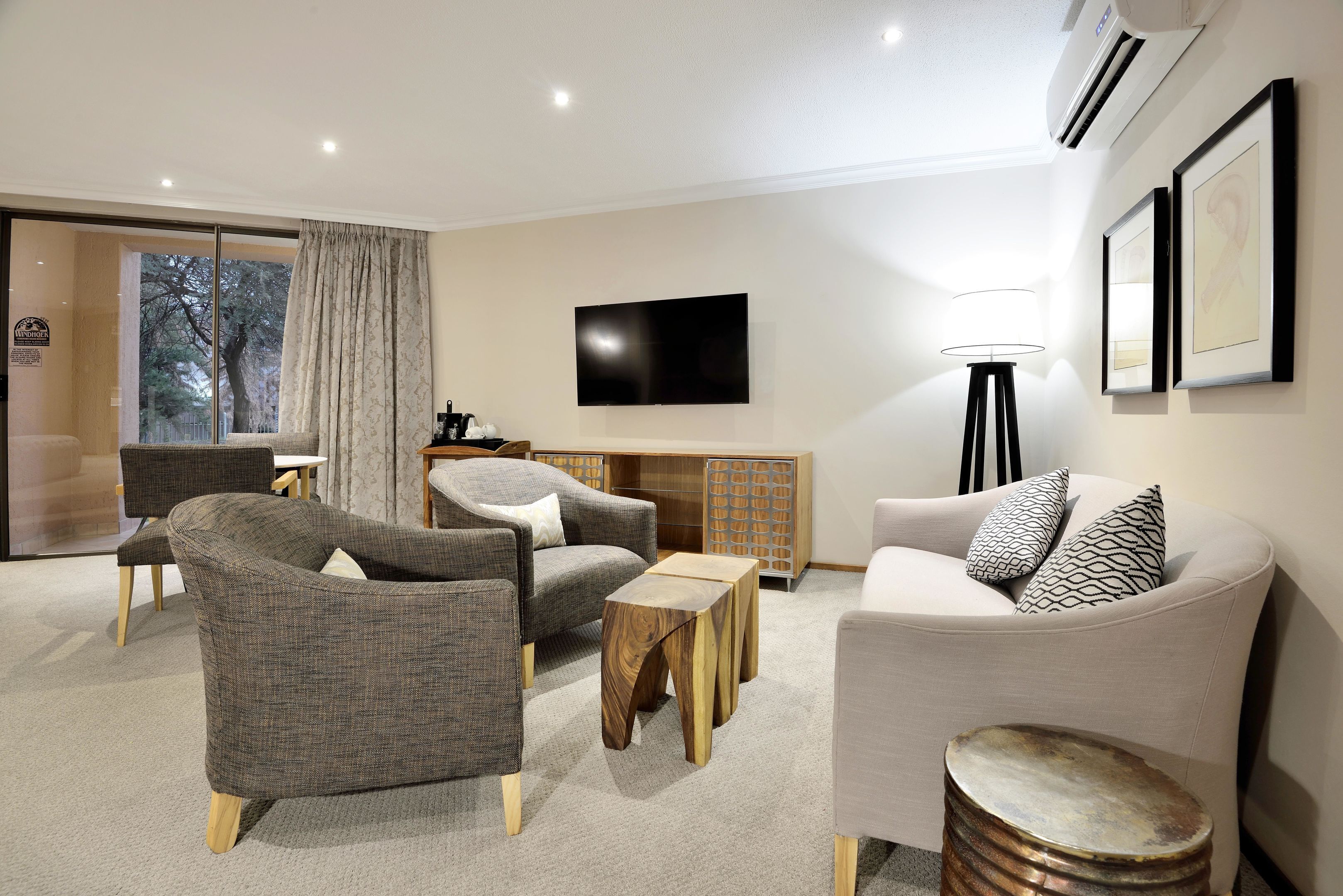 A modern living room with grey and white furniture, a flat-screen TV, and a large window with curtains.
