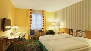 Quarto de hotel com duas camas, uma escrivaninha com telefone, uma cadeira, uma mesa pequena com abajur e uma televisão na parede.