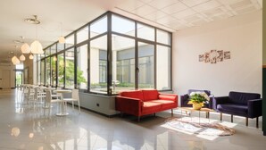 A spacious lobby with a modern design, featuring a red sofa, a purple armchair, and a coffee table with a vase of flowers. Large windows allow natural light to fill the space. - B&B Hotel Faenza (Faenza)