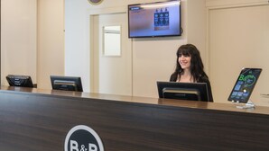 A reception desk with a B&B Hotels logo, a digital screen above, and a door in the background. - B&B Hotel Faenza (Faenza)