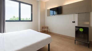 A hotel room with a bed, a small table, a TV mounted on the wall, and a window with curtains. - B&B Hotel Faenza (Faenza)