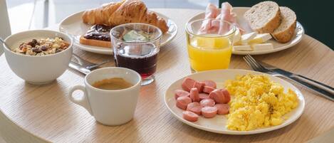 Una mesa de desayuno con croissants, huevos revueltos, salchichas y jugo.