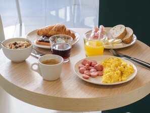 A breakfast table with croissants, scrambled eggs, sausages, and juice. - B&B Hotel Faenza (Faenza)