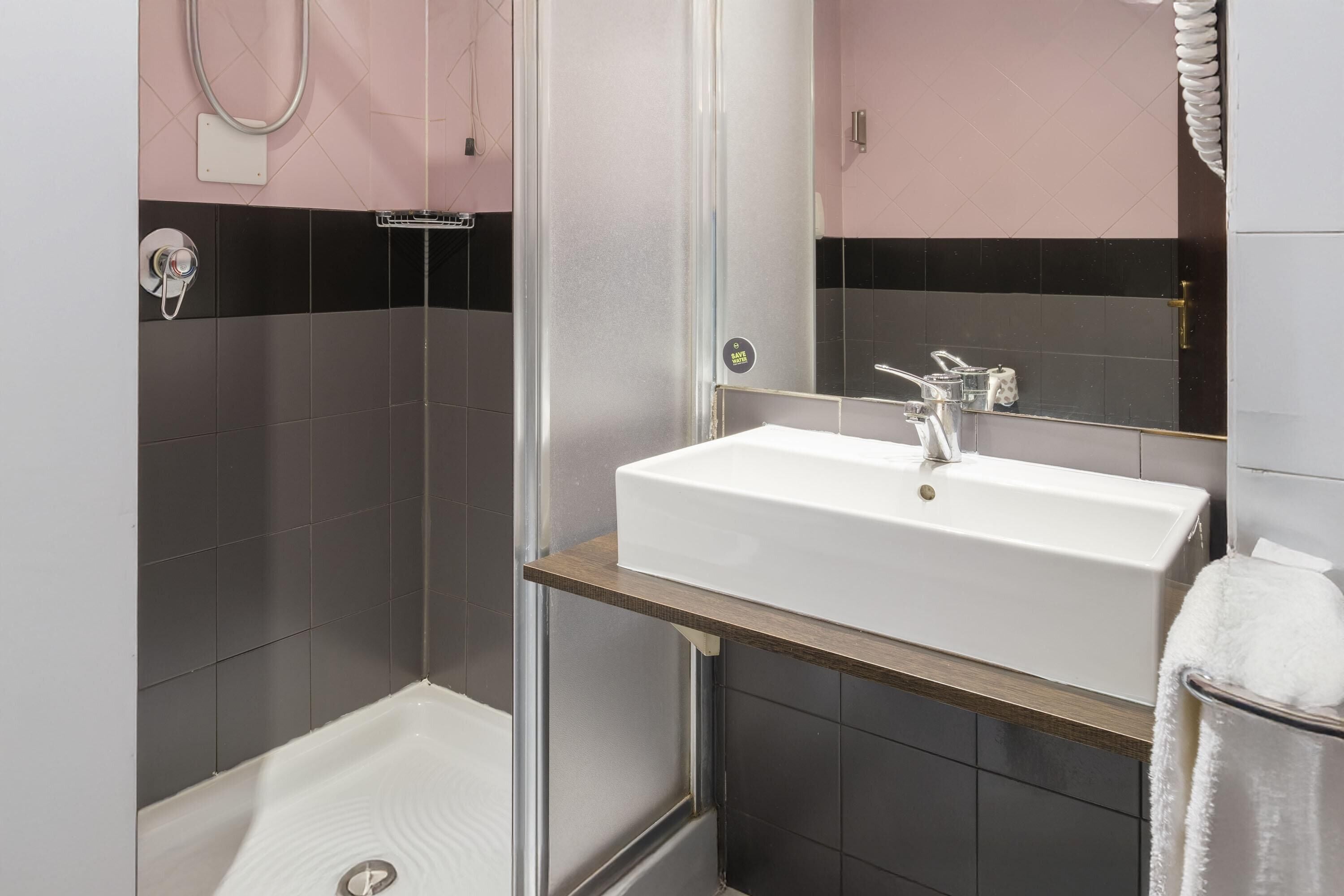 Ein modernes Badezimmer mit Waschbecken in Weiß, einer Duschkabine aus Glas und einem Handtuchhalter.