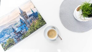 Un libro con una ilustración de un paisaje urbano, un plato blanco con una taza de café y un tapete gris redondo con una planta en maceta.