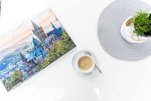 A book with a cityscape illustration, a white plate with a cup of coffee, and a round grey mat with a potted plant. - elaya hotel wolfenbuettel, Trademark Collection by Wyndham (Wolfenbuettel)