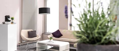 Ein modernes Wohnzimmer mit einer Couch, einem Sessel, einem Couchtisch und einer großen Topfpflanze.