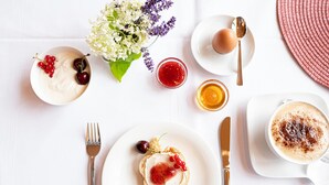 A breakfast setting with a plate of toast topped with cream and berries, a cup of coffee with cinnamon, and a bowl of yogurt with cherries. - elaya hotel wolfenbuettel, Trademark Collection by Wyndham (Wolfenbuettel)