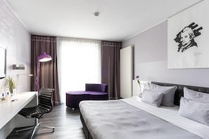 A hotel room with a bed, a desk, a chair, a lamp, and a window with curtains. - elaya hotel wolfenbuettel, Trademark Collection by Wyndham (Wolfenbuettel)