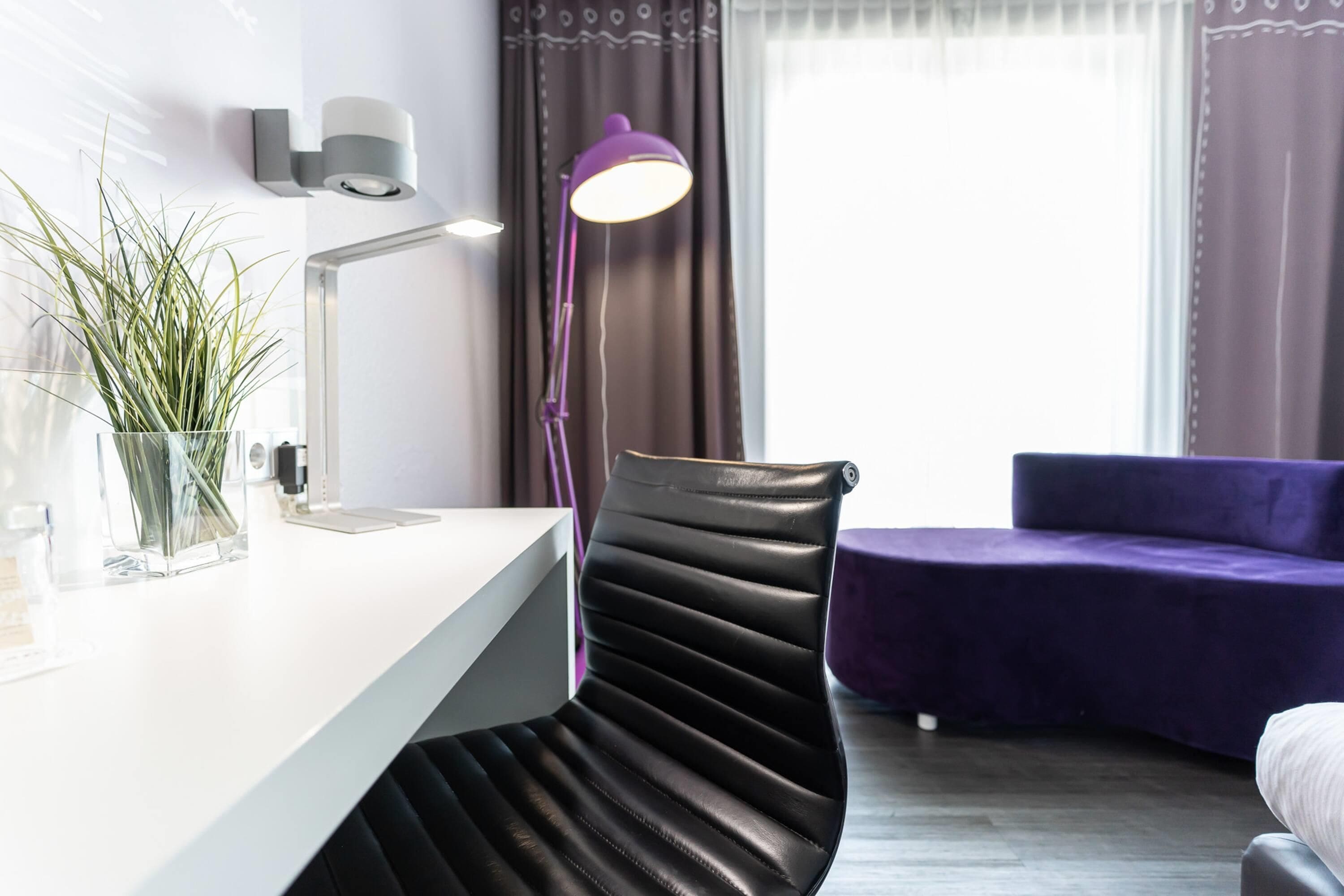 A modern room with a desk, a chair, a purple sofa, and a window with curtains.