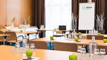A conference room with tables, chairs, a laptop, a projector screen, and decorative elements like apples and vases.