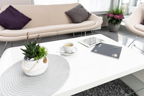 A modern living room with a white sofa, a coffee table with a potted plant, a tablet, and a smartphone. - elaya hotel wolfenbuettel, Trademark Collection by Wyndham (Wolfenbuettel)