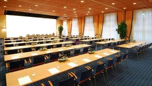 A conference room with multiple tables and chairs, arranged in a U-shape, with a large screen at the front. - elaya hotel wolfenbuettel, Trademark Collection by Wyndham (Wolfenbuettel)