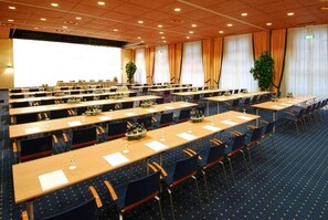 A conference room with multiple tables and chairs, arranged in a U-shape, with a large screen at the front. - elaya hotel wolfenbuettel, Trademark Collection by Wyndham (Wolfenbuettel)
